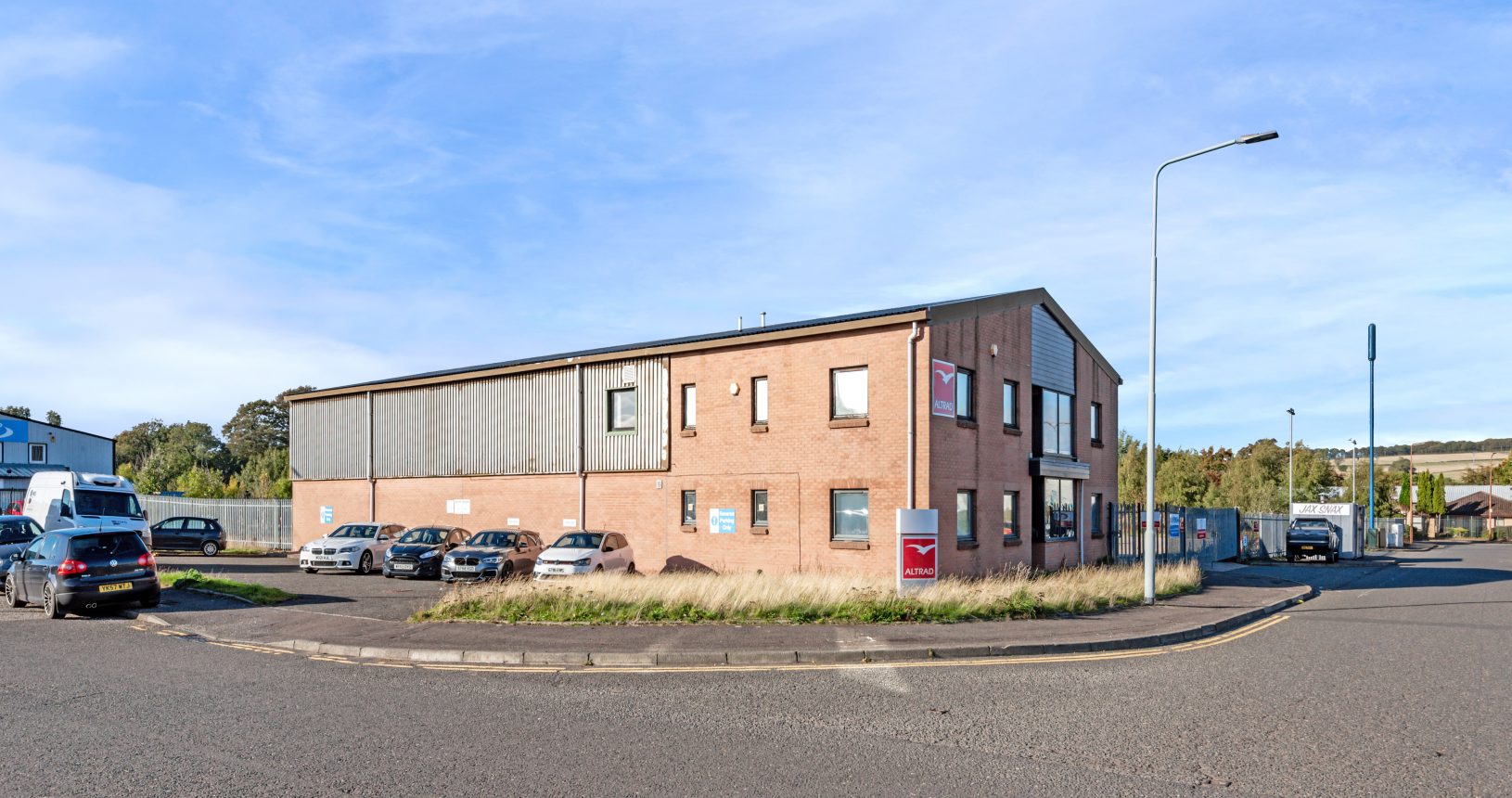 Two-storey industrial and office building at Mill Road Industrial Estate in Linlithgow with forecourt parking and countryside backdrop.