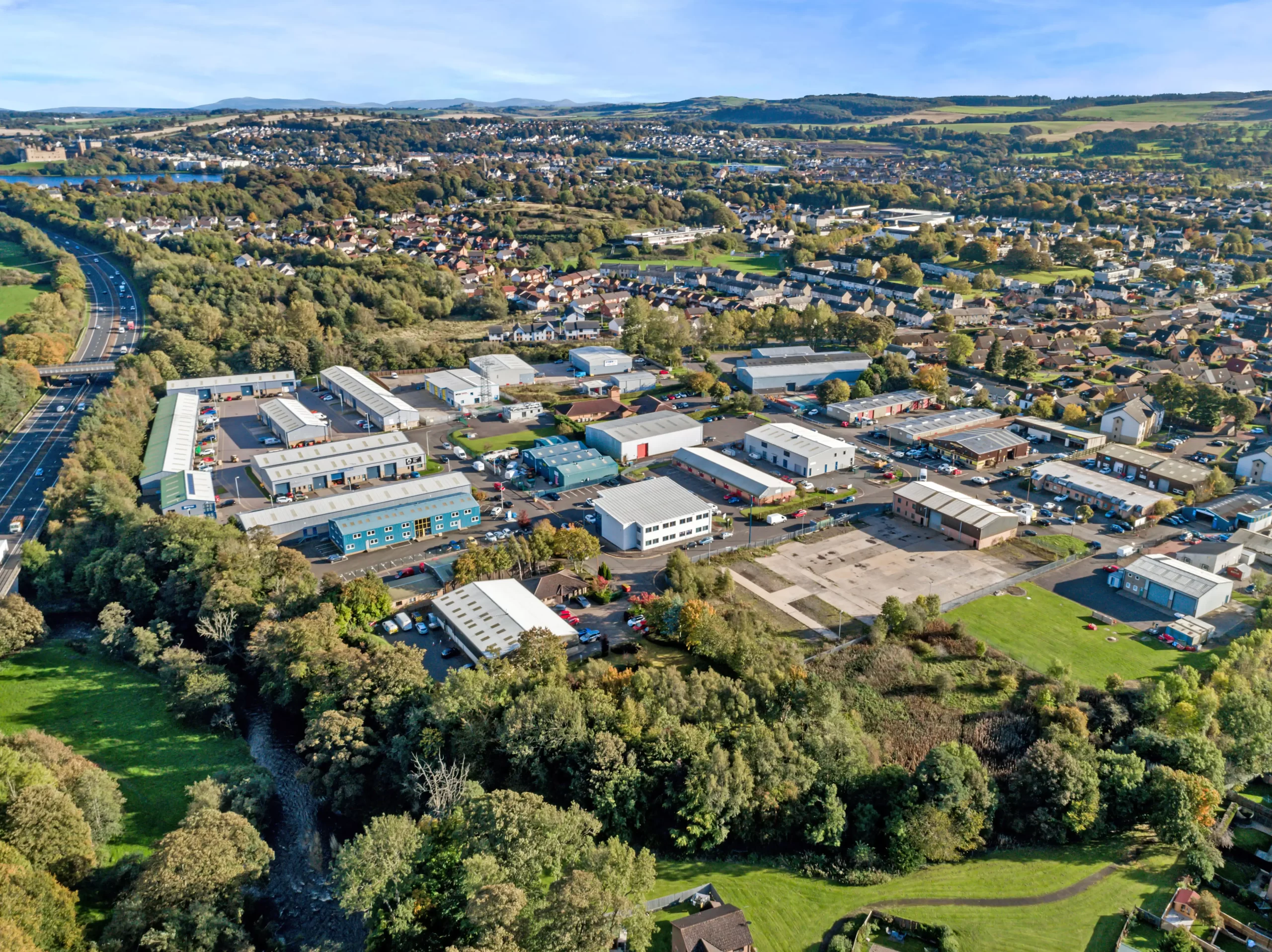 Aerial view of an industrial estate Linlithgow showing Mill Road Industrial Estate with surrounding businesses, road access, and green landscape.