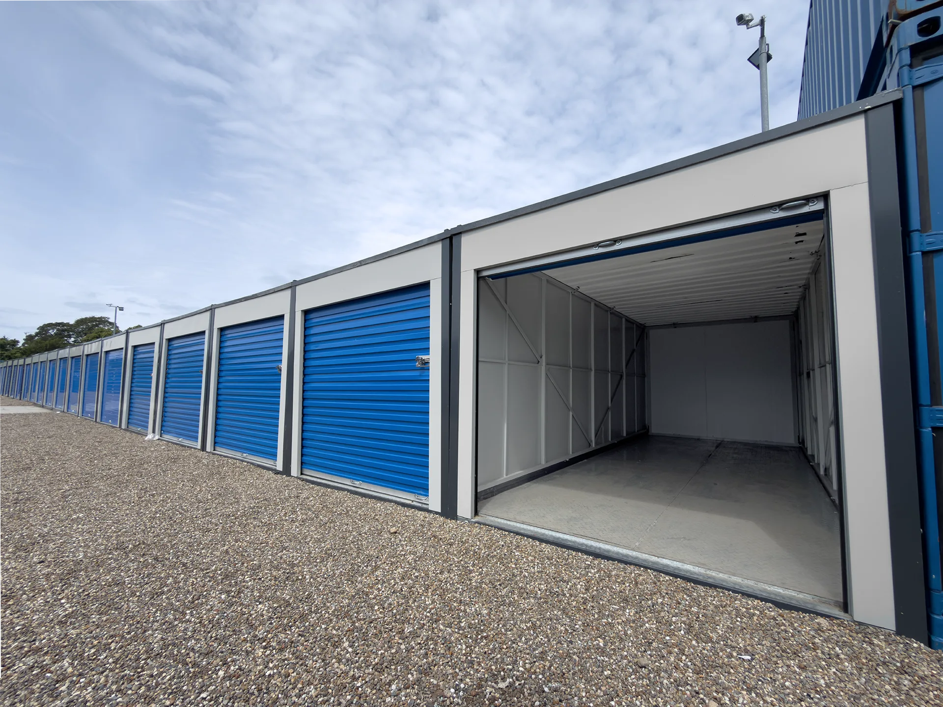 Drive-up Strongholds storage units in Linlithgow with blue roller doors and an open storage unit.